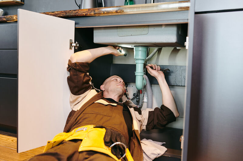 Professional plumber fixing new pipe under sink with wrench